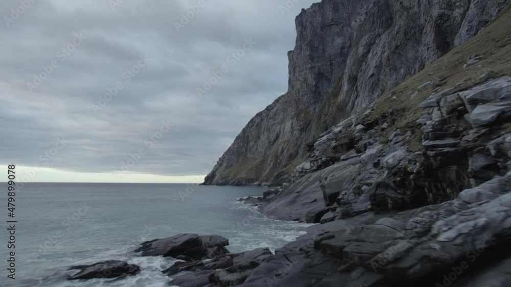 Aerial drone view low over the rocky coast, under steep mountains, gloomy evening, in Lofoten, Norway Aerial drone view low over the rocky coast, under steep mountains, gloomy evening, in Lofoten, Norway