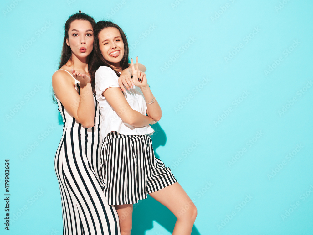 Two young beautiful smiling blond hipster female in trendy summer clothes. Sexy carefree women posing near blue wall in studio. Positive models having fun. Cheerful and happy Two young beautiful smiling blond hipster female in trendy summer clothes. Sexy carefree women posing near blue wall in studio. Positive models having fun. Cheerful and happy