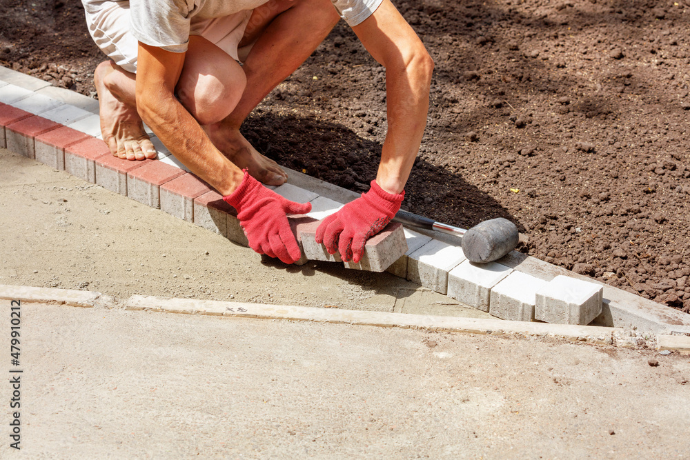A worker lays paving slabs on a park path on a bright sunny day. A worker lays paving slabs on a park path on a bright sunny day.