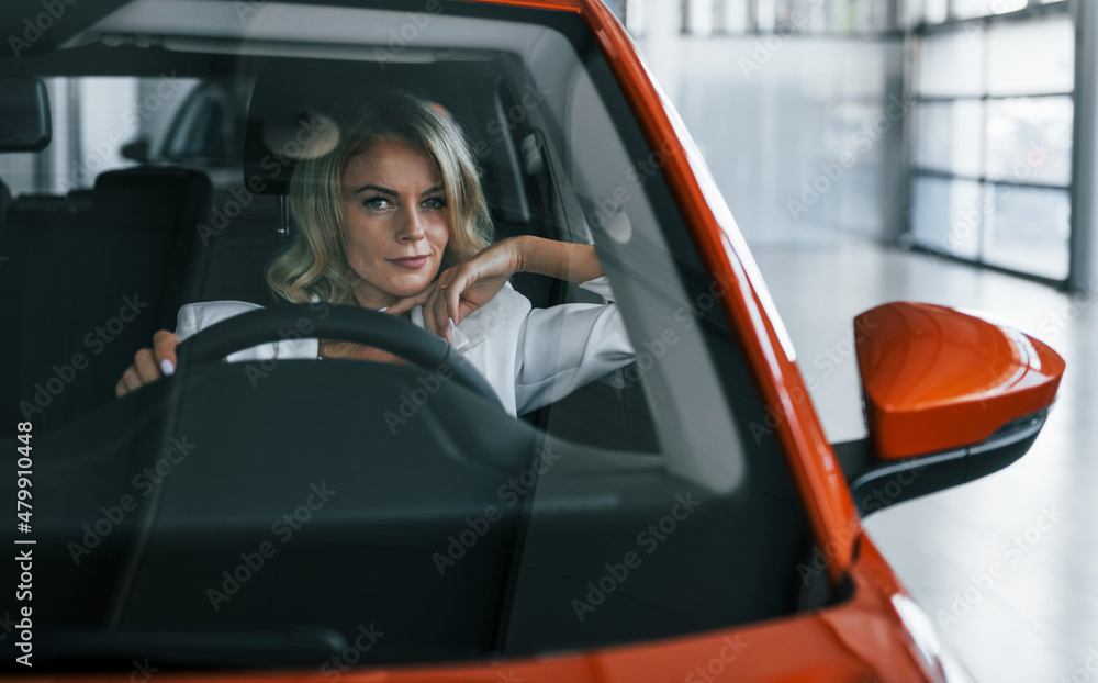 Sitting in the car. Woman in formal clothes is indoors in the autosalon