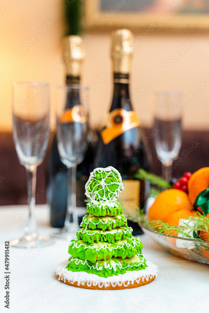 Gingerbread in the form of a Christmas tree with green glaze on a New Year's table against a background of champagne