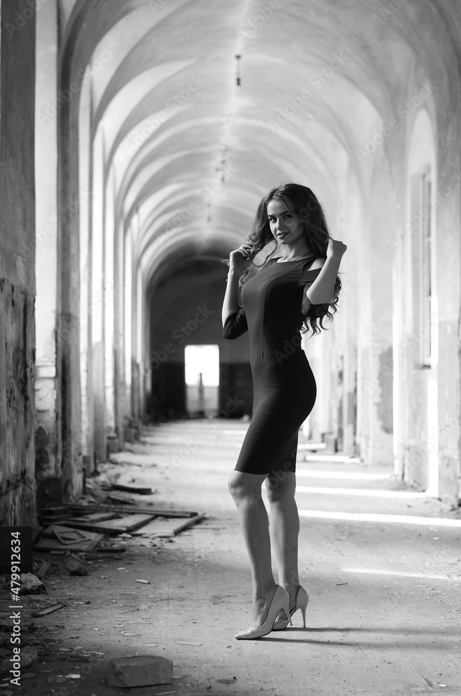 Young beautiful short hair blonde woman in black climbing the stairs, black and white photo. Side view of elegant romantic mysterious lady with movie star look in interior with bricks walls