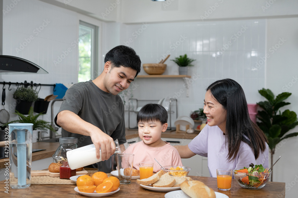 Asian family breakfast at home. Parents and children enjoy eating together, talking with laughter and good atmosphere. Father and mother plays with son playfully at kitchen table. Asian family breakfast at home. Parents and children enjoy eating together, talking with laughter and good atmosphere. Father and mother plays with son playfully at kitchen table.