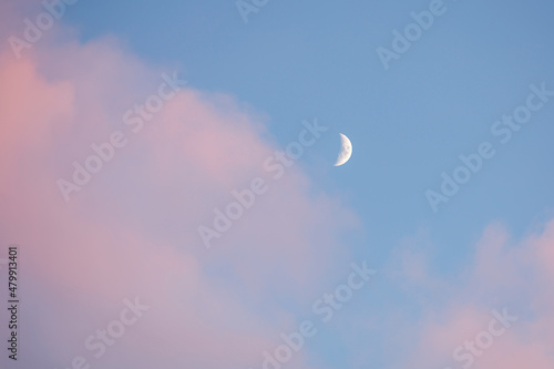 Half moon white on a blue sky with pink clouds. Young moon on a beautiful pastel heavens