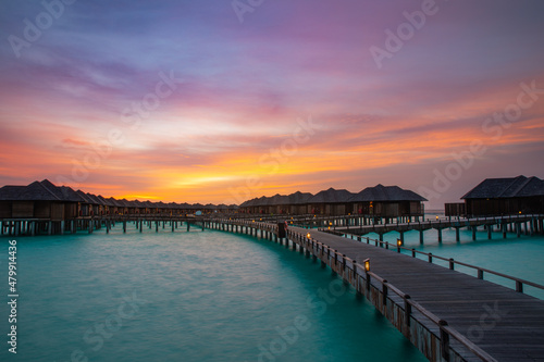 Amazing sunset panorama at Maldives. Luxury resort villas seascape with soft led lights under colorful sky. Dramatic twilight sky and colorful clouds. Beautiful beach background for vacation holiday