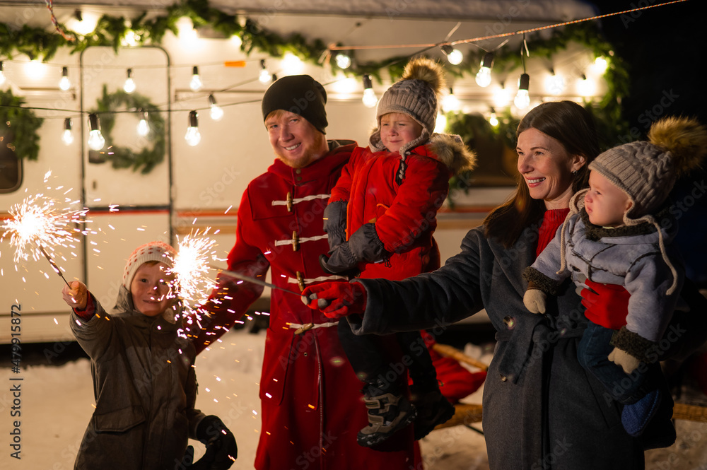 Obraz premium Happy family celebrates christmas in nature and holds sparklers. Parents with three sons travels in a van.