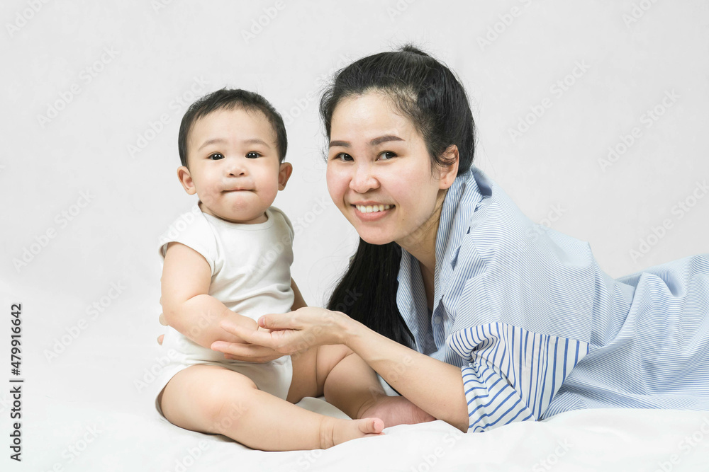 Happy young asian mother lying and holding adorable baby's hand with love and caring on the blanket at home, looking at the camera on white background Happy young asian mother lying and holding adorable baby's hand with love and caring on the blanket at home, looking at the camera on white background