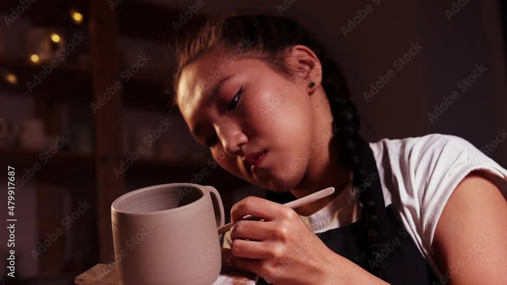 Pottery in the studio - woman holding a cup on the plate and smearing parts of clay on the joint on the handle and a cup Pottery in the studio - woman holding a cup on the plate and smearing parts of clay on the joint on the handle and a cup