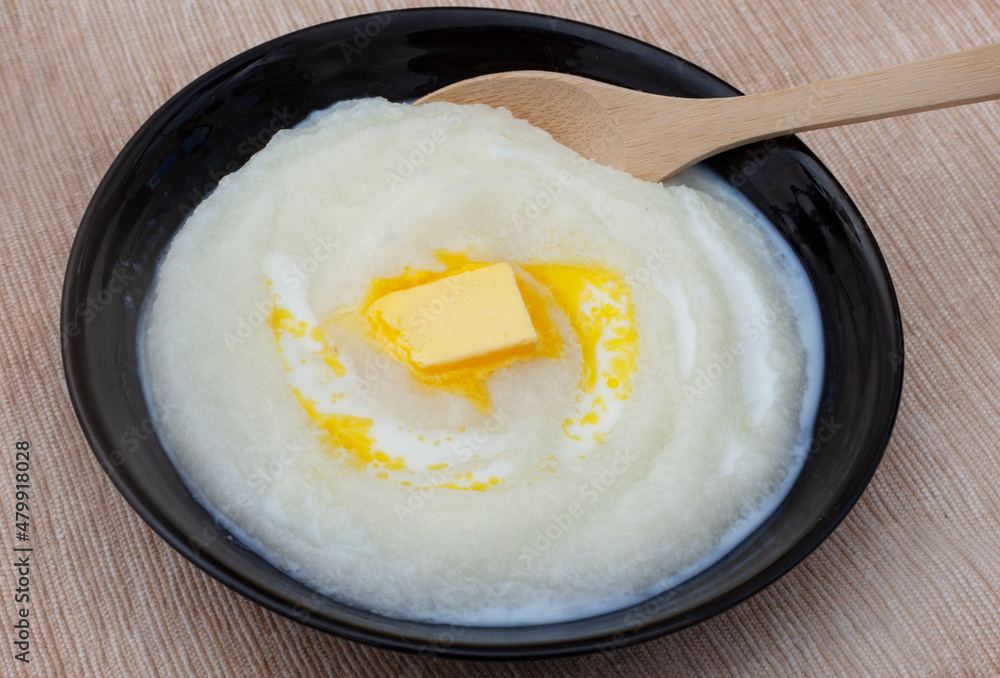 Traditional South African Maize meal porridge in black bowl on rustic background with wooden spoon and melting block of butter Traditional South African Maize meal porridge in black bowl on rustic background with wooden spoon and melting block of butter