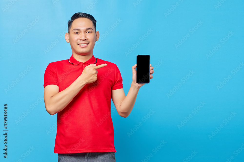 Portrait of smiling young asian man pointing fingers at blank screen mobile phone isolated on blue background Portrait of smiling young asian man pointing fingers at blank screen mobile phone isolated on blue background