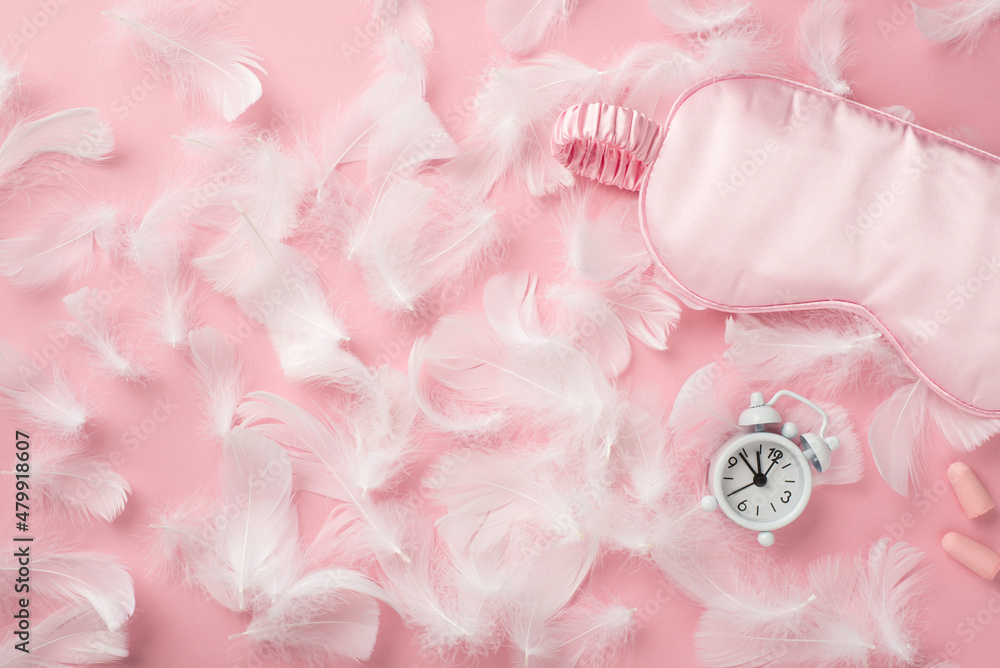 Top view photo of small white alarm clock light pink satin sleeping mask earplugs and pink feathers on isolated pastel pink background with copyspace Top view photo of small white alarm clock light pink satin sleeping mask earplugs and pink feathers on isolated pastel pink background with copyspace
