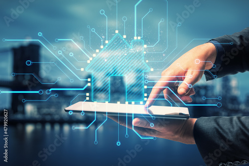 Close up of businessman hand pointing at tablet with abstract glowing house chip hologram on blurry night city background. Smart home, ai and information concept. Double exposure.