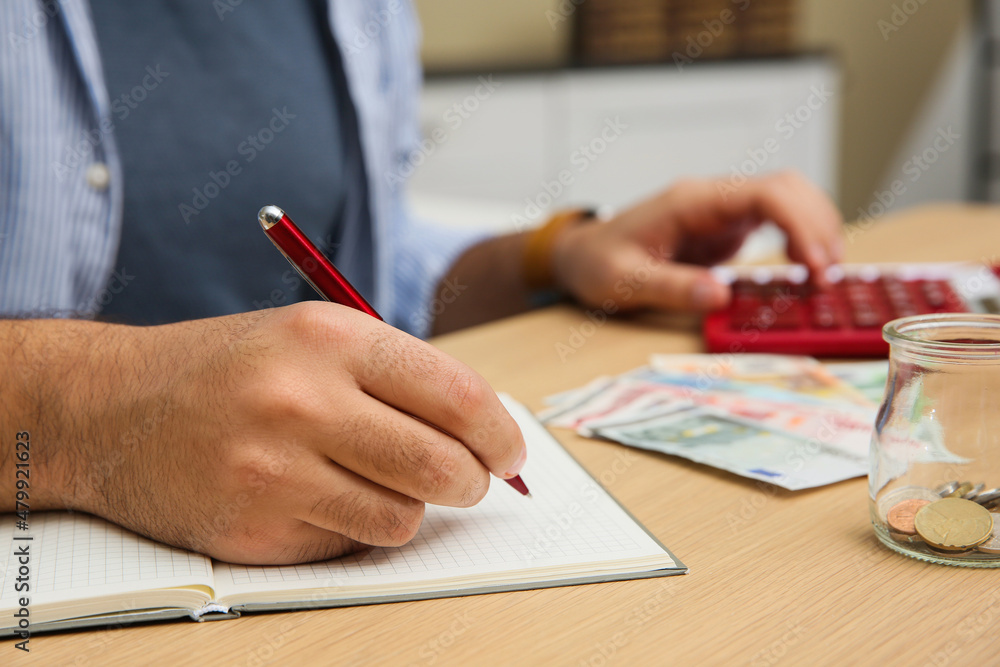 Man counting money with calculator at table indoors, closeup Man counting money with calculator at table indoors, closeup