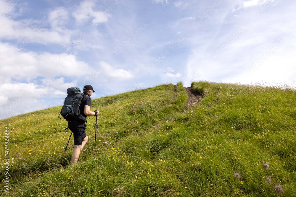 Hiker with backpack and hiking poles climbing a green hill