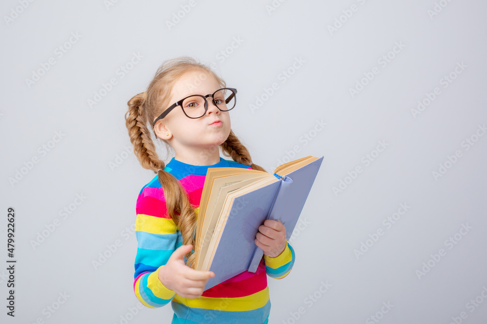 a cute little girl in a multicolored sweater and glasses holds a book on a white background , smiling a cute little girl in a multicolored sweater and glasses holds a book on a white background , smiling