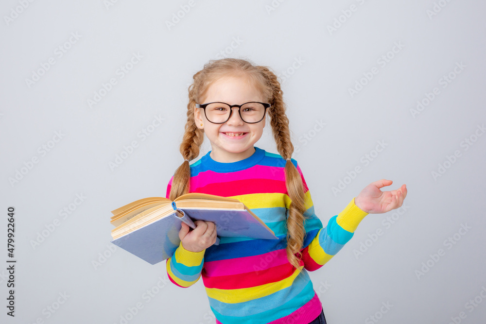 a cute little girl in a multicolored sweater and glasses holds a book on a white background , smiling a cute little girl in a multicolored sweater and glasses holds a book on a white background , smiling