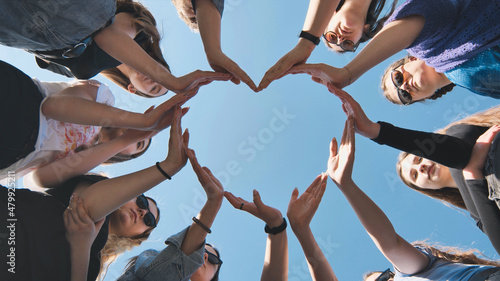 Cheerful girlfriends make a heart shape out of their hands.