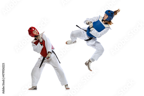 Dynamic portrait of two young women, taekwondo practitioners training together isolated over white background. Concept of sport, skills