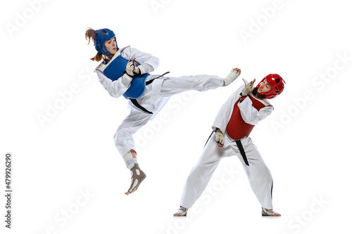 Dynamic portrait of two young women, taekwondo practitioners training together isolated over white background. Concept of sport, skills