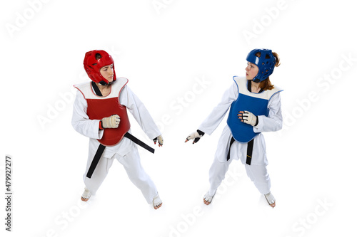 Studio shot of of two young women, taekwondo athletes practicing together isolated over white background. Concept of sport, skills
