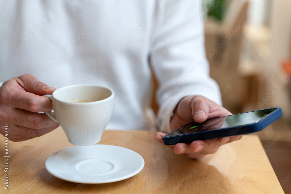 Cropped view of the caucasian guy recording message while sitting at cafeteria with cup of coffee Cropped view of the caucasian guy recording message while sitting at cafeteria with cup of coffee