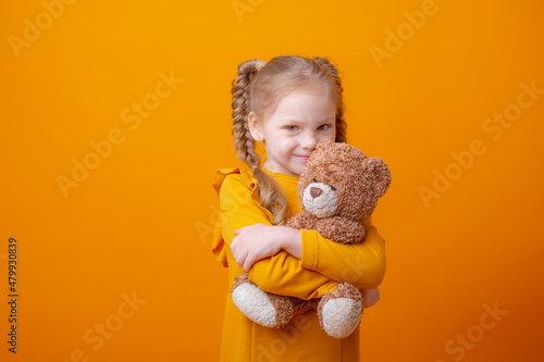 Foto cute little girl holding a teddy bear on a yellow background, hugging