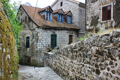 an old stone ancient European city street, ends with a small house with green shutters, a red tiled roof