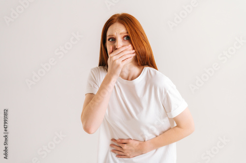 Portrait of unwell young woman feeling painful cramp in stomach, grimacing and writhing in pain feeling stomach ache indigestion, periods miscarriage, on white isolated background in studio.