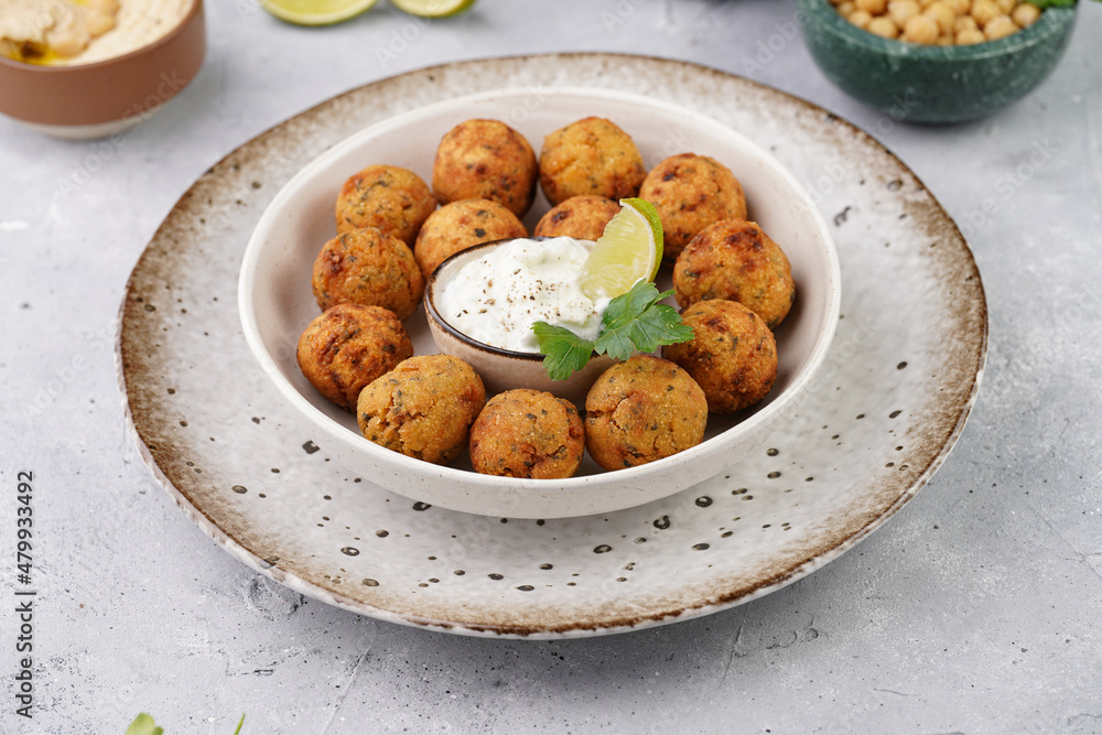 Traditional oriental chickpea deep fried falafel in a deep bowl with tzatziki yoghurt sauce, hummus, fresh lime and green cilantro on light grey concrete surface Traditional oriental chickpea deep fried falafel in a deep bowl with tzatziki yoghurt sauce, hummus, fresh lime and green cilantro on light grey concrete surface