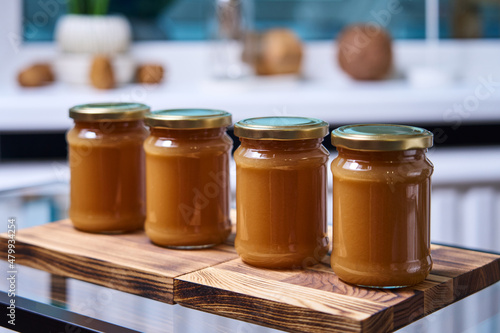 jars of homemade caramel are on a wooden stand on a glass table