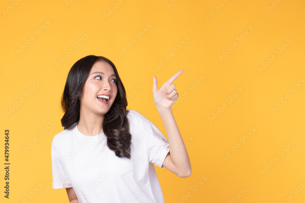 Beautiful Asian woman wearing casual clothes smile and pointing finger at copy space isolated on yellow background studio portrait. Beautiful Asian woman wearing casual clothes smile and pointing finger at copy space isolated on yellow background studio portrait.