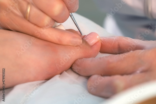 Pedicurist master is applying shiny soft pink gel shellac on woman's toes in beauty clinic using thin brush, closeup view. Hygiene and care for feet. Professional pedicure in cosmetology clinic.