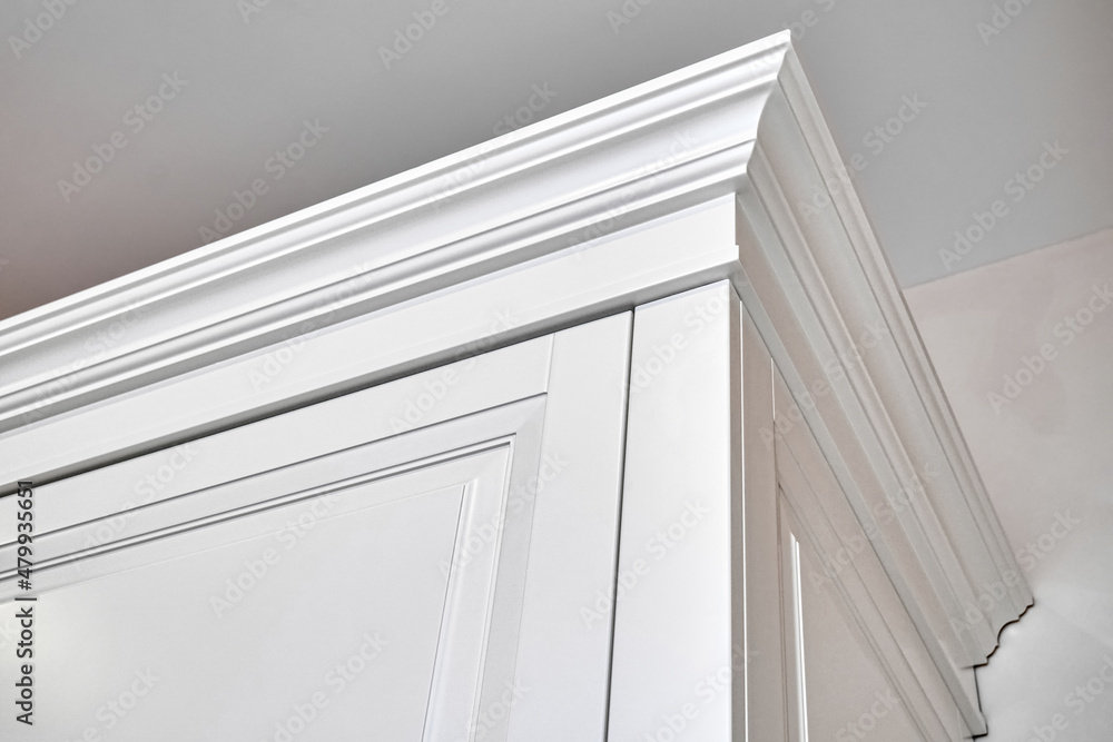 Obraz premium Crown moldings of elegant white vintage wardrobe cabinet in classic style in light empty room in luxury apartment closeup