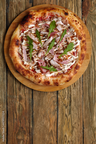 neapolitan Pizza with Mozzarella cheese, bacon, ham, tomato sauce, chicken, Spices and Fresh arugula. Italian pizza on wooden table background