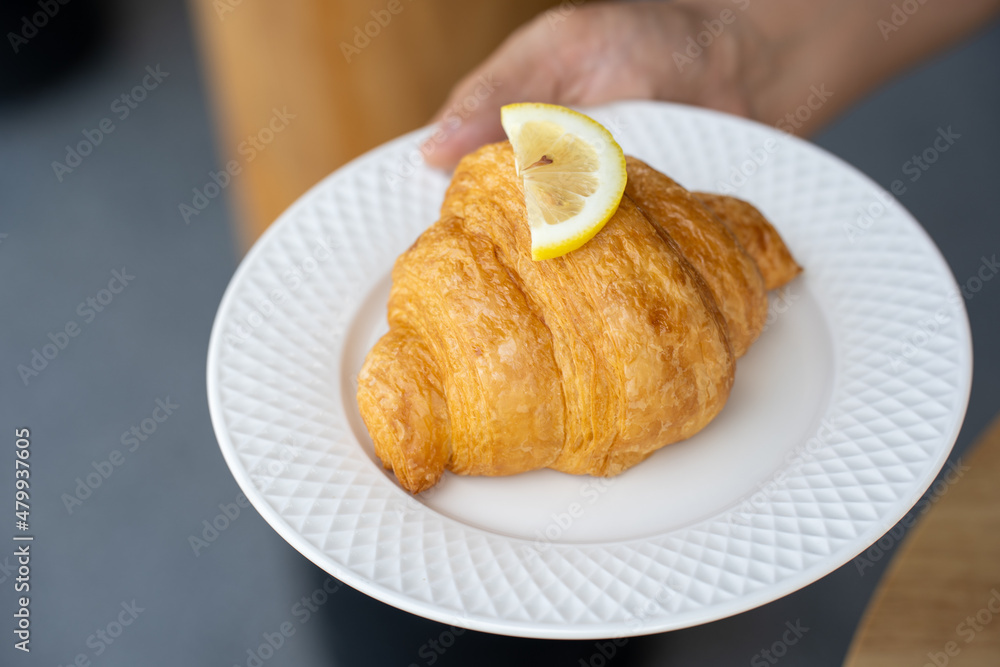 Yuzu croissant on a white ceramic plate holding a woman's hand Yuzu croissant on a white ceramic plate holding a woman's hand