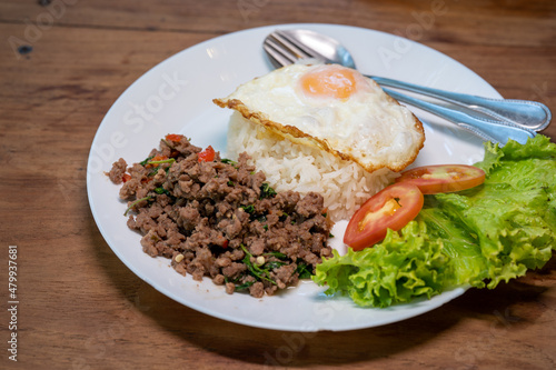 Beef basil fried rice, fried egg on top, on wooden table, popular food of Thailand.
