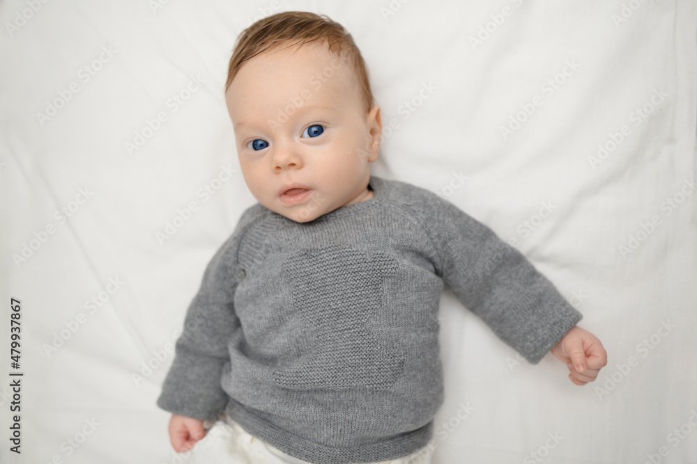 Portrait of lovely baby with blue eyes lying in bed. Baby smiling and looking up to camera. Good morning. Beautiful baby boy four months old lying on a blue soft blanket. Portrait of lovely baby with blue eyes lying in bed. Baby smiling and looking up to camera. Good morning. Beautiful baby boy four months old lying on a blue soft blanket.