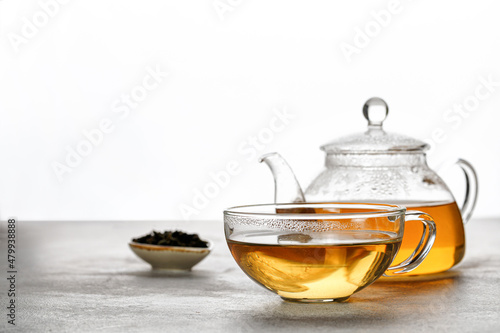 A mug or cup with green herbal tea and a teapot with tea leaves on grey background. Beauty color