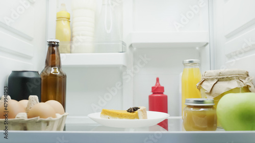 tasty cake, eggs, apple, bottles with drinks, sauces, honey and fruit puree in refrigerator.