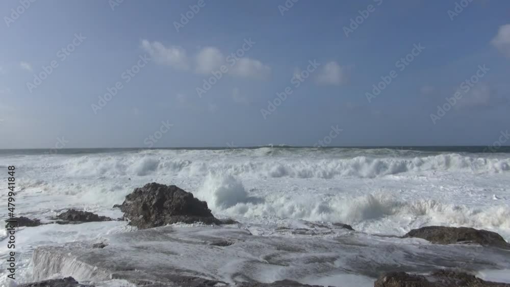 Ocean coast with rolling waves, sea foam and salt water splashes, rocky coast of the Atlantic Ocean, windy weather in the sea, blue sky above the sea, volcanic stones near the seashore Ocean coast with rolling waves, sea foam and salt water splashes, rocky coast of the Atlantic Ocean, windy weather in the sea, blue sky above the sea, volcanic stones near the seashore