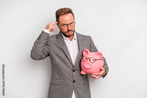 middle age man feeling confused and puzzled, showing you are insane. businessman and a pigy bank concept photo