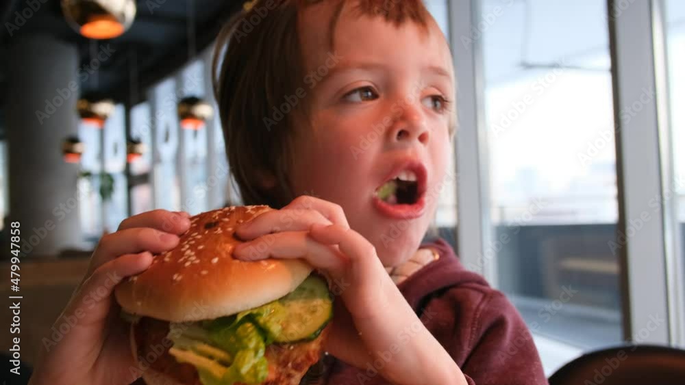 Little boy in fast food cafe eats burger. Portrait of hungry child Cute little kid eating burger. Hungry child in fast food cafe. Close-up boy eating burger. Hungry child in cafe. Lovely boy Little boy in fast food cafe eats burger. Portrait of hungry child Cute little kid eating burger. Hungry child in fast food cafe. Close-up boy eating burger. Hungry child in cafe. Lovely boy