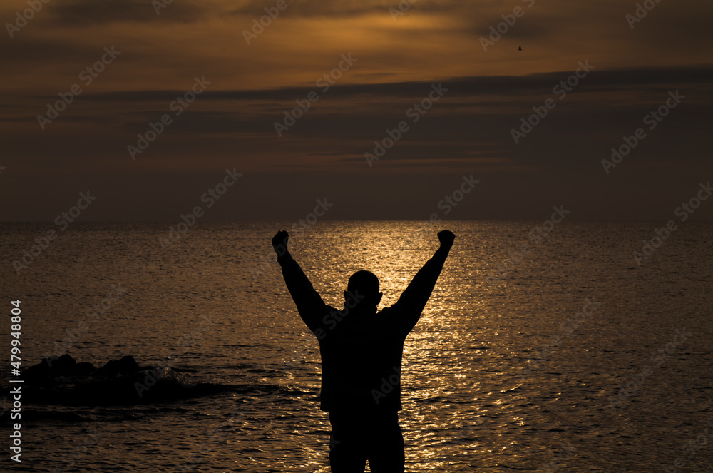 Silhouette of adult man raising arms looking at sea during sunset. Almeria, Spain