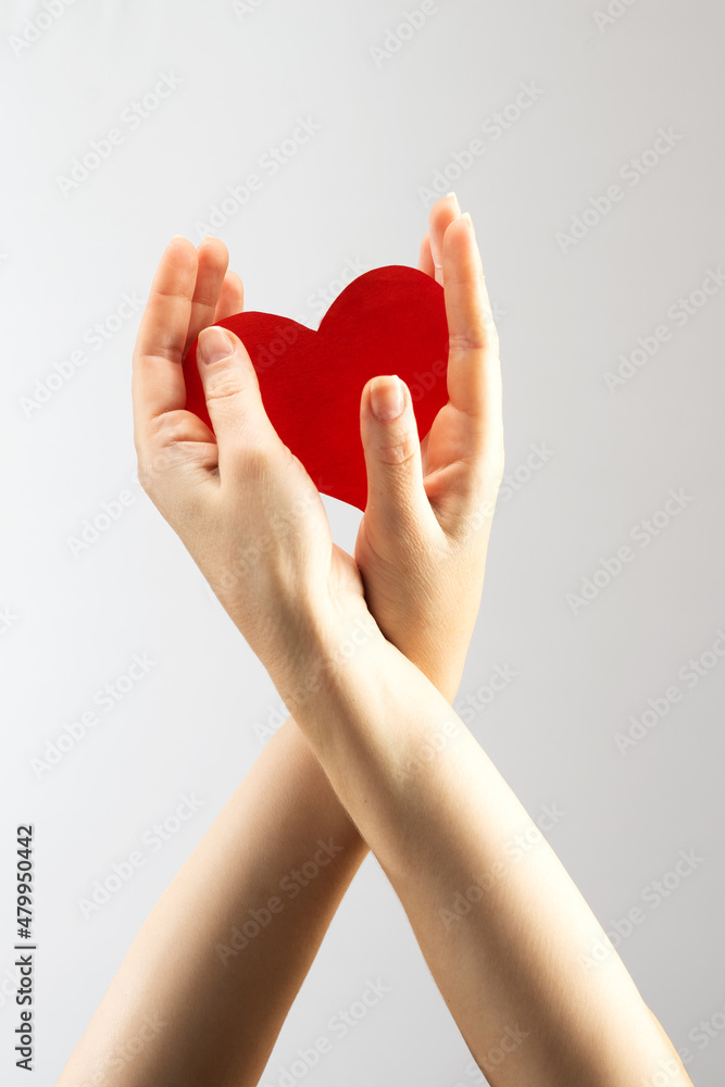 Fototapeta premium Female hand holding a red heart on a white background. Health care and medicine concept. AIDS awareness
