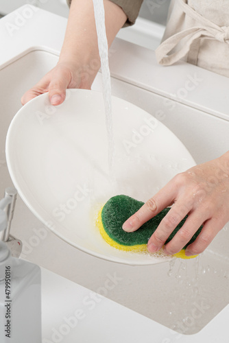 Fotografie Woman housekeeper is doing the dishes at home kitchen.