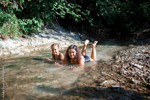 Happy girl with her mother bathing in stream canyon river in the mountains  nature pool. Cold water  hardening and natural spa procedure  wildlife and green tourism  summer holidays