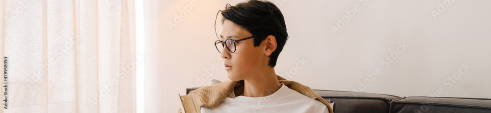 Asian boy in eyeglasses looking aside while resting on bed Asian boy in eyeglasses looking aside while resting on bed