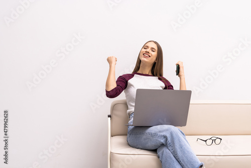 Portrait of happy woman sitting on floor and looking at laptop screen, holding phone and card, checking bank account, winning lottery, crediting a large amount of money. © F8  \ Suport Ukraine