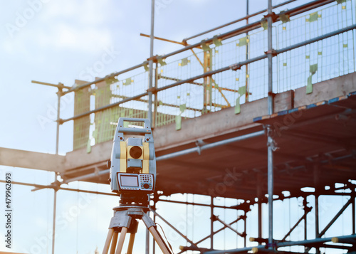 Total station set by engineer on construction site in front of scaffolds installed around new house