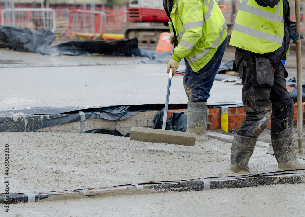 Construction workers pouring wet self leveling concrete screed during ground floor construction of a new residential house and spreading it with spazzle Construction workers pouring wet self leveling concrete screed during ground floor construction of a new residential house and spreading it with spazzle
